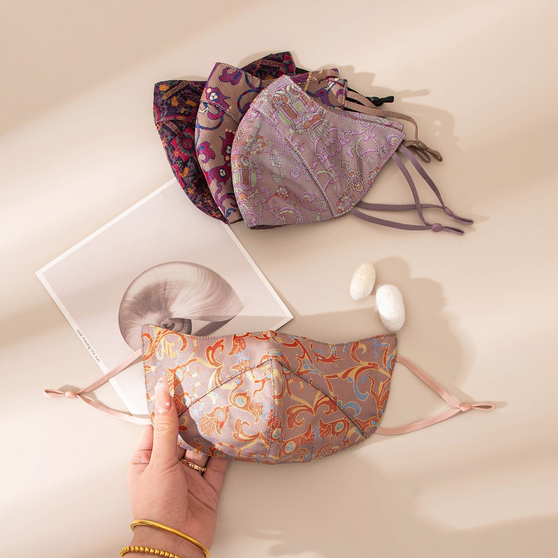 Handmade Song brocade silk face coverings in plum, lilac and coral patterns on an editorial desk